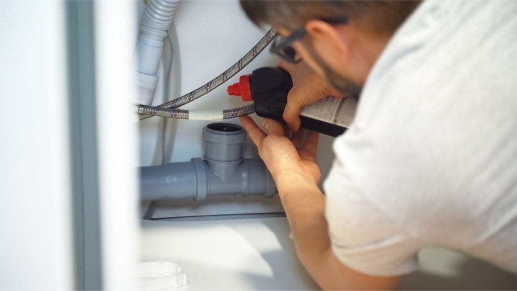 Plumber repairing PVC drainage pipes under a sink.