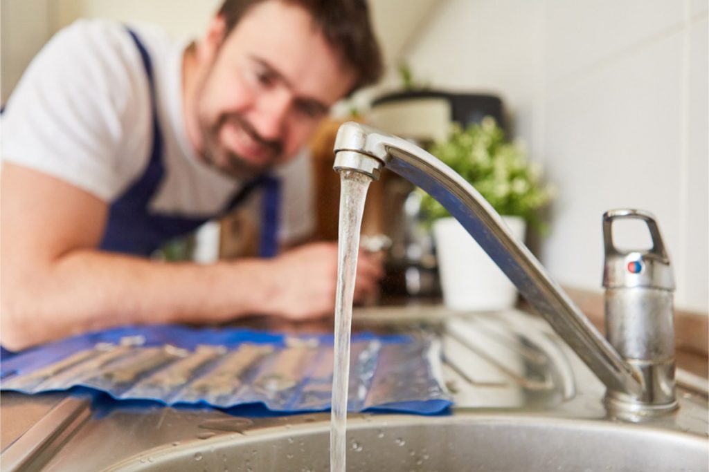 Plumber inspecting water flow from a kitchen sink tap.